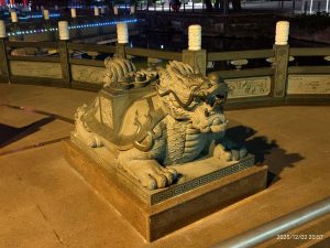 蓮池潭夜間景觀中，一尊巨大的石雕麒麟造型雕像位於欄杆前。