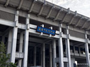 高雄市文化中心建築外觀，上方設有藍底白字的標牌，上方有層次感的屋頂結構。