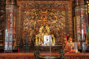 四湖參天宮內殿，金身神像供奉於繁複木雕神龕前，兩側立玻璃櫃文物