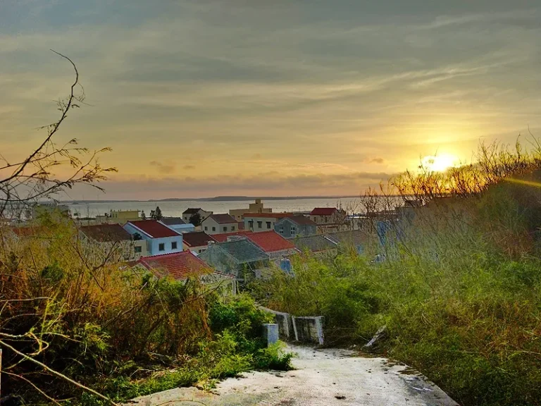 員貝嶼夕陽，金黃落日映照海面，紅瓦村落與草坡沐浴在暮色中