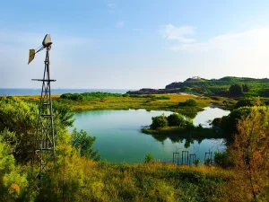 澎湖山水濕地公園，風車旁碧綠潭水倒映藍天與海岸