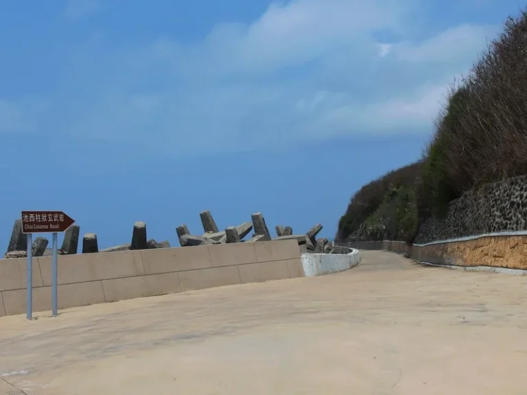 池西岩瀑入口，水泥產業道路旁立著紅色指示牌與消波塊海堤
