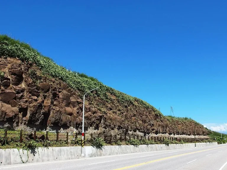 青灣玄武岩，公路旁邊坡裸露紅褐色柱狀玄武岩節理，藍天遼闊