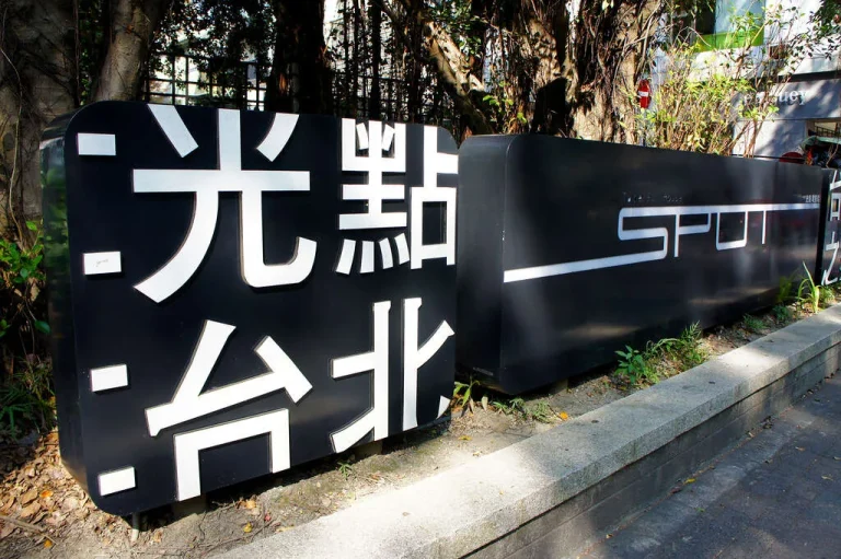SPOT光點台北電影館，黑色招牌以白字標示光點台北與SPOT字樣立於樹下