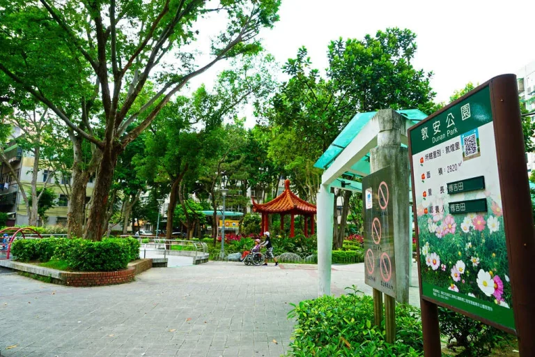 臺北市敦安公園，綠樹圍繞的紅磚廣場與紅頂涼亭及解說牌