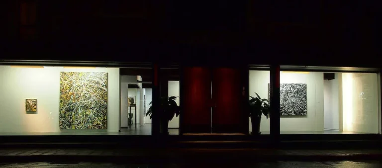 赤粒藝術，夜間玻璃櫥窗內透出燈光的抽象畫作與盆栽門面
