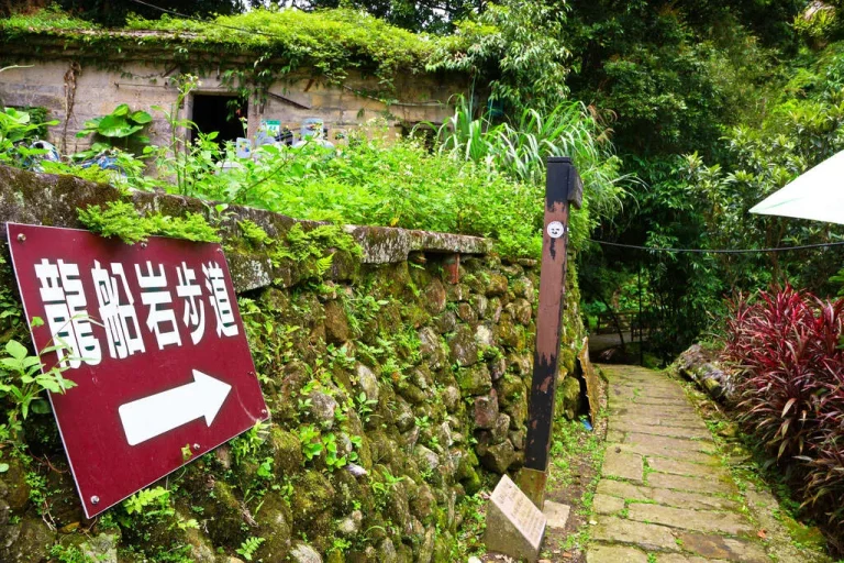 臺北市龍船岩步道，紅底白字指示牌立於石牆旁，後方石階沒入山林