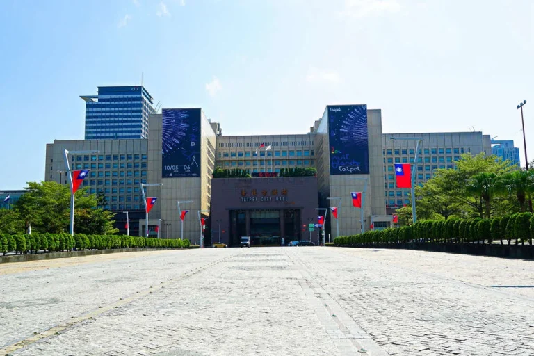 臺北市政府大樓，棕色磚牆建築前廣場插滿國旗，藍天晴朗