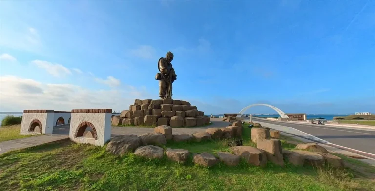 漁翁島遊客中心，草坡上人物石雕立於石砌拱廊基座，遠方跨海大橋橫越