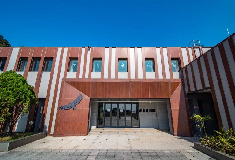 觀音山猛禽展示館，紅褐色直紋外牆建築正面，門口有猛禽圖案裝飾