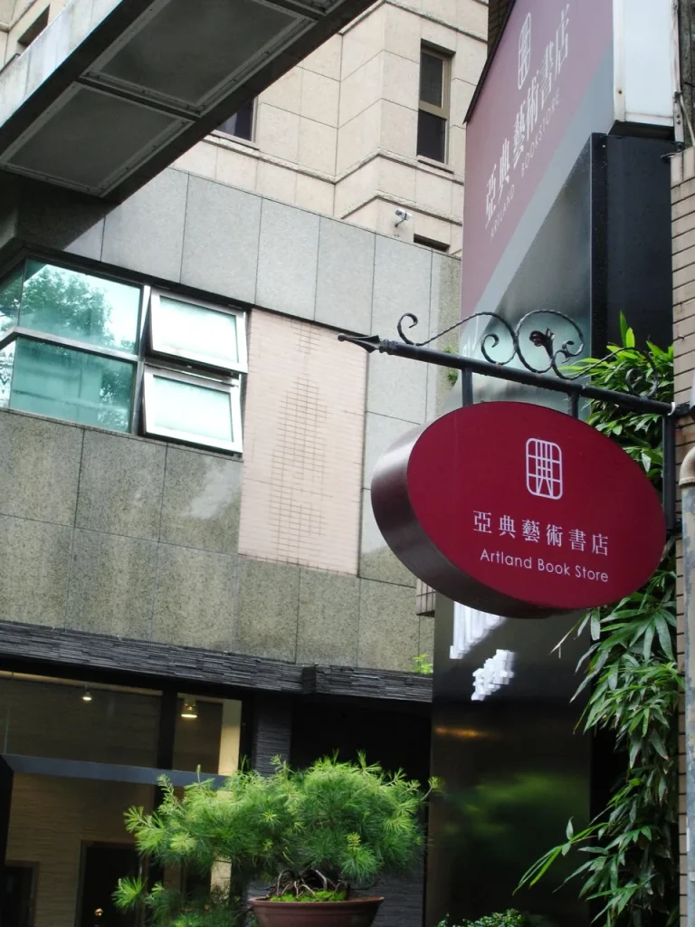亞典藝術書店，巷弄建築外懸掛的紅色橢圓書店招牌與盆栽
